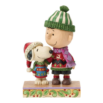 Jim Shore Peanuts Cozy Christmas Pals figurine featuring Snoopy and Charlie Brown wearing matching Christmas sweaters, scarves, and winter hats with colorful folk-art holiday details.