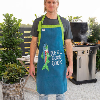 Fun Graphic Aprons & Oven Mitts Kitchen Essentials Collection at Chivilla Bay. Pictured Reel Good Cook BBQ Apron in backyard BBQ setting.