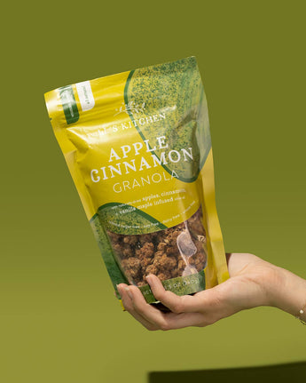 Hand holding a package of Apple Cinnamon Granola against a green background