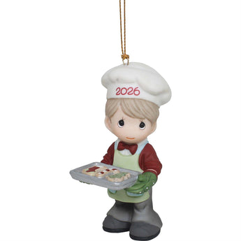 Precious Moments ornament of a boy in a chef's outfit with '2026' on his hat, holding a tray of cookies.