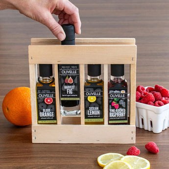 Wooden gift box with Olivelle olive oil bottles on a wooden surface with fruits and lemons.