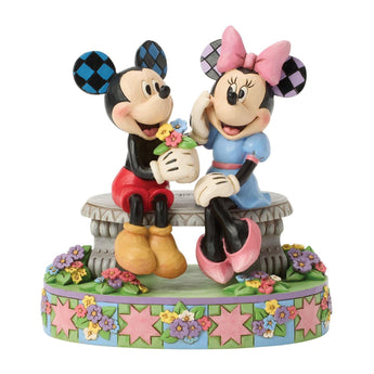 Jim Shore Disney Traditions "A Blooming Romance" figurine featuring Mickey presenting Minnie with flowers on a park bench surrounded by colorful spring details.