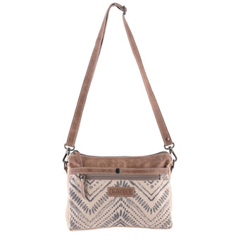 Neutral-toned canvas and leather crossbody bag with tribal pattern and adjustable strap, featuring front zipper and stitched leather details.