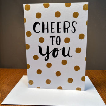Greeting card with 'Cheers to You' text and gold polka dots on a white background