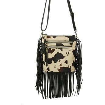 Cow print crossbody bag with black fringe on a white background