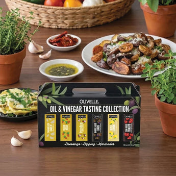 Olivelle Italian Olive Oil and Vinegar Tasting Gift Set with six 50 ml bottles in a gift box with different food dishes in background and cloves of garlic and herbs.