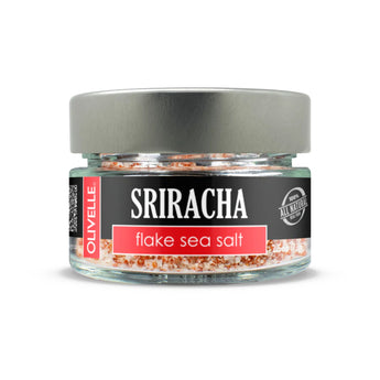 Glass jar of Olivelle's Sriracha Flake Sea Salt - bold red seasoning perfect for adding spice to any dish.