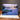 Happy Anniversary Greeting card with a scenic illustration of a dock and sunset over water on a wooden surface.