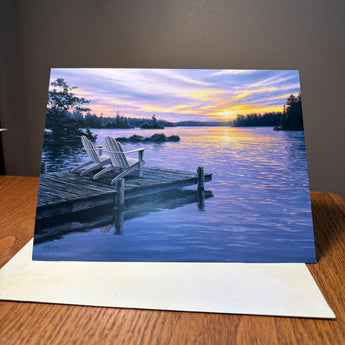 Happy Anniversary Greeting card with a scenic illustration of a dock and sunset over water on a wooden surface.