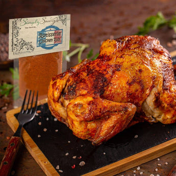 Roasted chicken on a cutting board with a container of Rodisserie Chicken Rub and a fork.