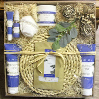 Gift set with Laze Spa products including body lotion, bath bombs, and a woven basket on a wooden surface.