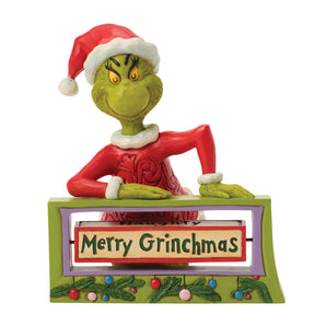 Grinch figurine with 'Merry Grinchmas' sign on a white background