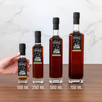Four bottles of Olivelle toasted sesame oil with varying sizes on a wooden surface.