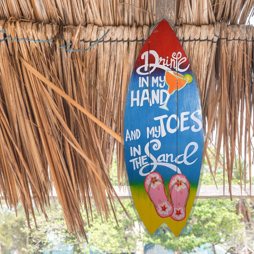 Surfboard-shaped sign in vibrant colors with 'Drink in my hand and toes in the sand', flip flops and margarita design.