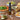 A bottle of Olivelle Garlic & Herb olive oil stands on a wooden table surrounded by food props including a pizza, salads, bread, garlic, and pasta, creating a warm, appetizing scene.