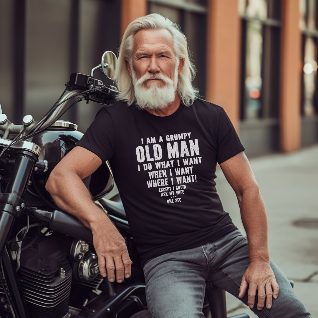 Humorous 'Grumpy Old Man' graphic tee featuring text: 'I am a grumpy old man, I do what I want, when I want, where I want! Except I gotta ask my wife...one sec.' Available in various colors.