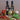 Three olive oil bottles from Olivelle on a wooden surface, surrounded by fresh and dried ingredients including a red tomato, cherry tomatoes, basil, garlic, and dried red pepper flakes.