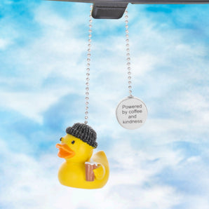 Yellow Duck Charm with coffee and beanie and sentiment tag that reads 'powered by coffee and kindness' hanging from car mirror.