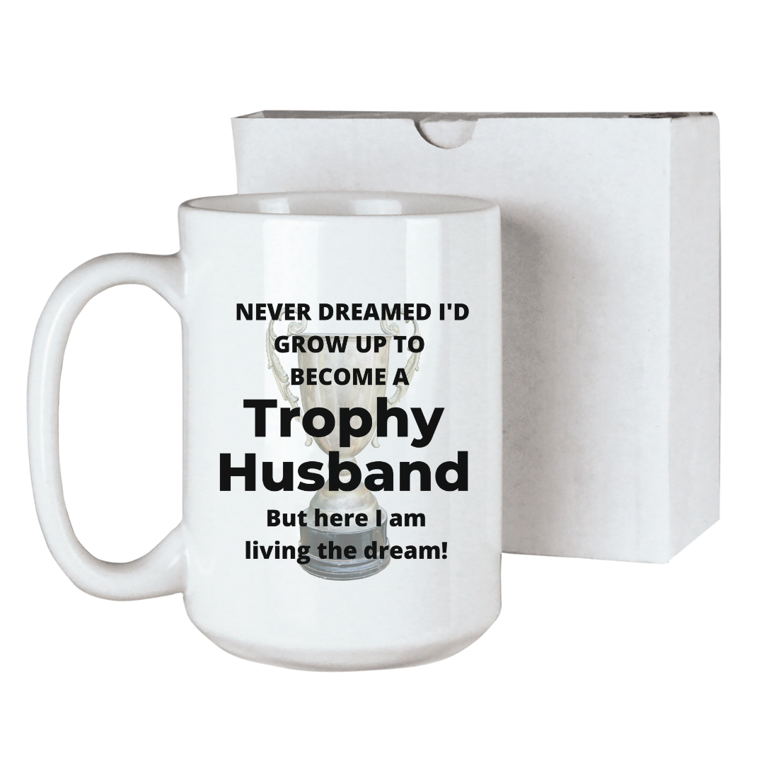 Trophy husband funny coffee mug with a trophy in the background and the text "Never dreamed I'd grow up to become a Trophy husband, but here I am living the dream!" sublimated onto a 15 ounce ceramic coffee mug. Comes with a gift box. Funny gift for his birthday or anniversary.