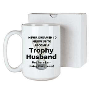 Trophy husband funny coffee mug with a trophy in the background and the text "Never dreamed I'd grow up to become a Trophy husband, but here I am living the dream!" sublimated onto a 15 ounce ceramic coffee mug. Comes with a gift box. Funny gift for his birthday or anniversary.
