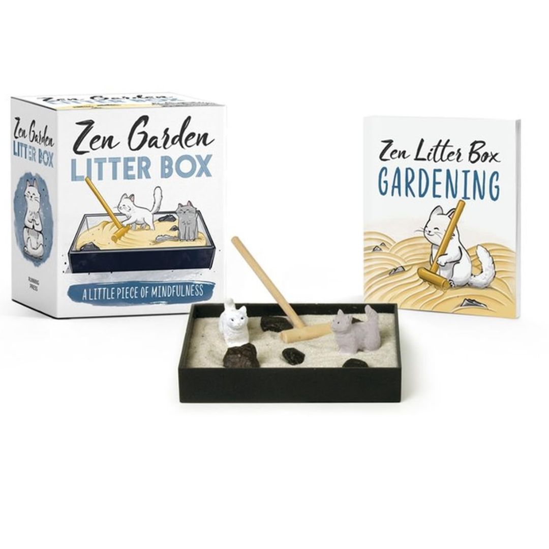 Miniature Zen garden litter box with two cat figurines, sand, decorative rocks, and a wooden rake, set on a calm workspace.