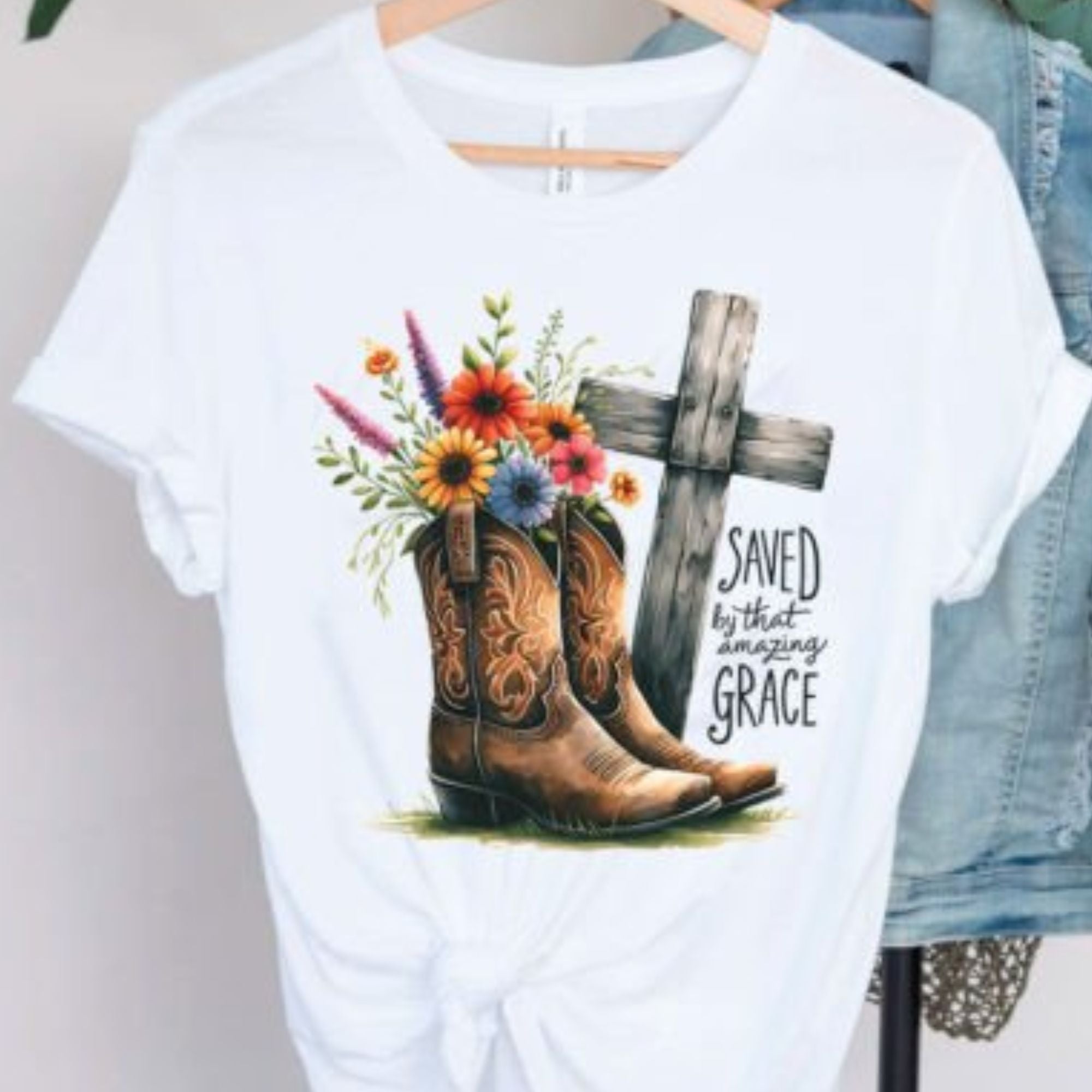White cotton t-shirt with 'Saved by That Amazing Grace' saying and a design of flowers in cowboy boots next to an old wooden cross, available at Chivilla Bay.