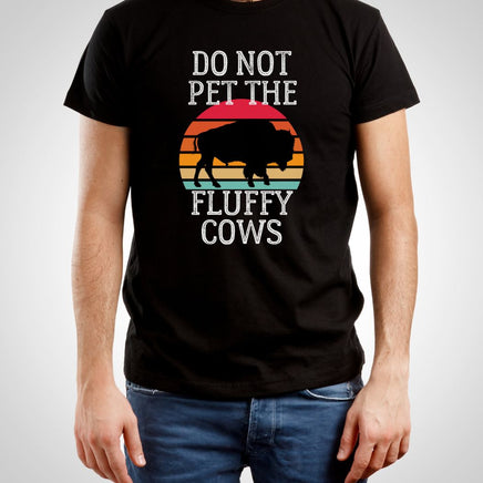 Man wearing a black 'Do Not Pet the Fluffy Cows' graphic t-shirt, featuring a bison/buffalo silhouette against a sunset horizon, direct-to-garment printed on a unisex cotton tee.